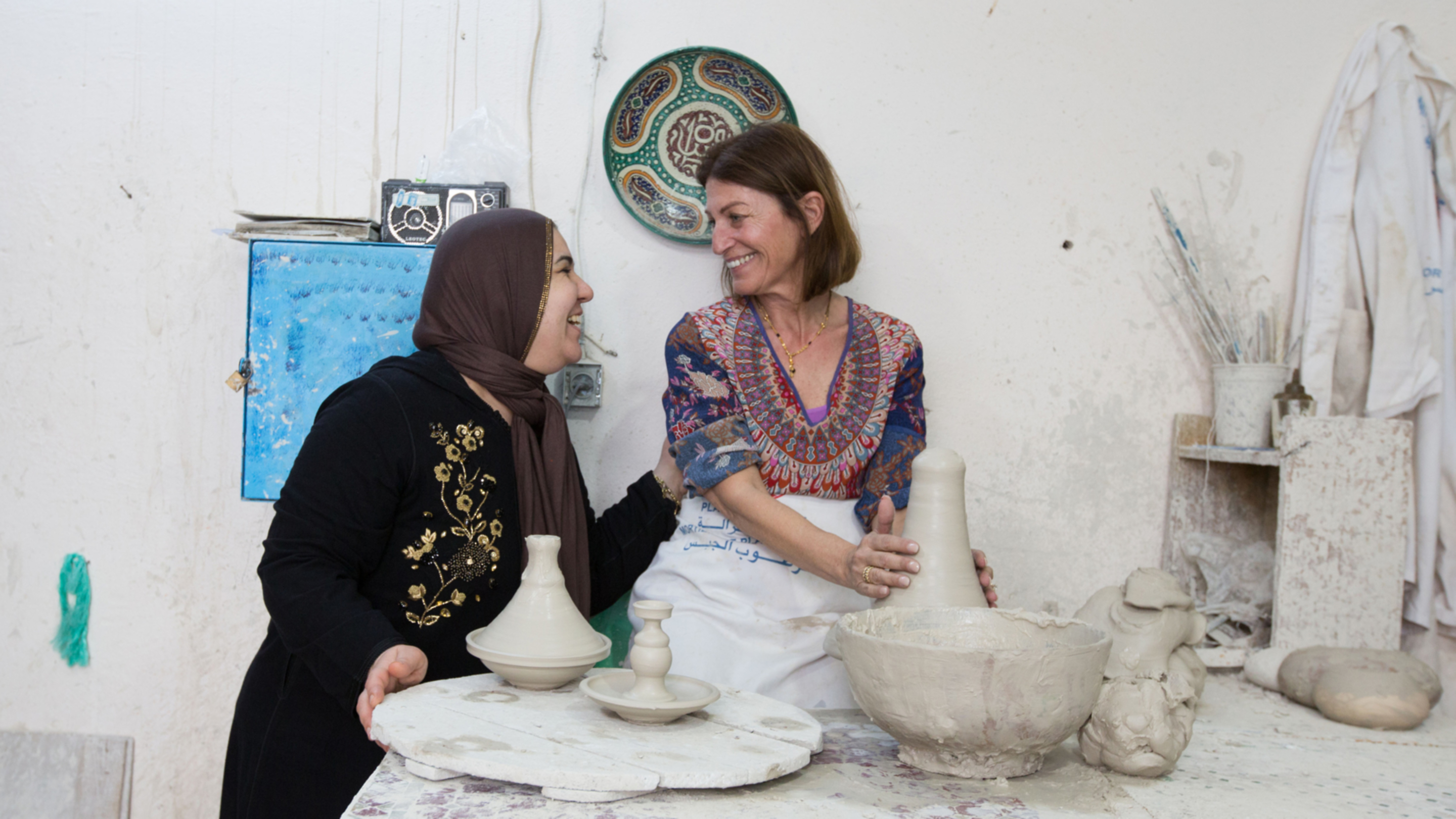 Woman enjoys making pottery with a local resident on her trip
